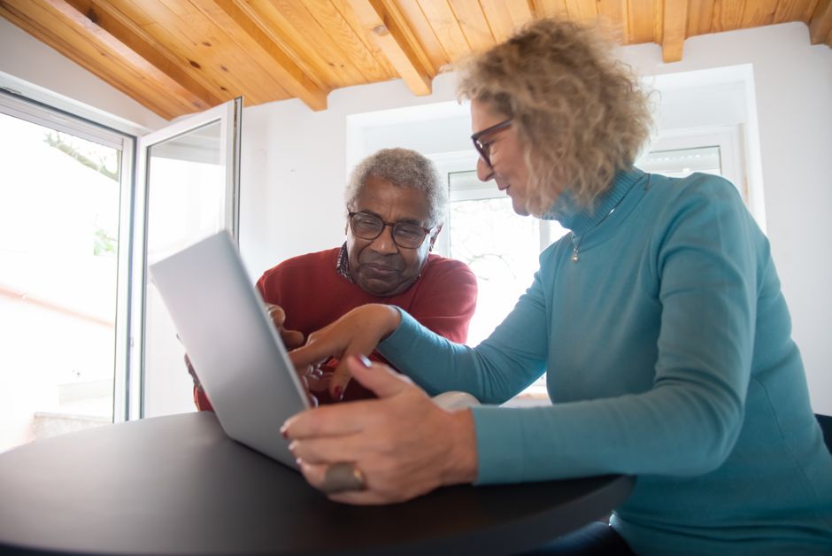 Elderly couple sitting together using a laptop to fill in a travel application at home