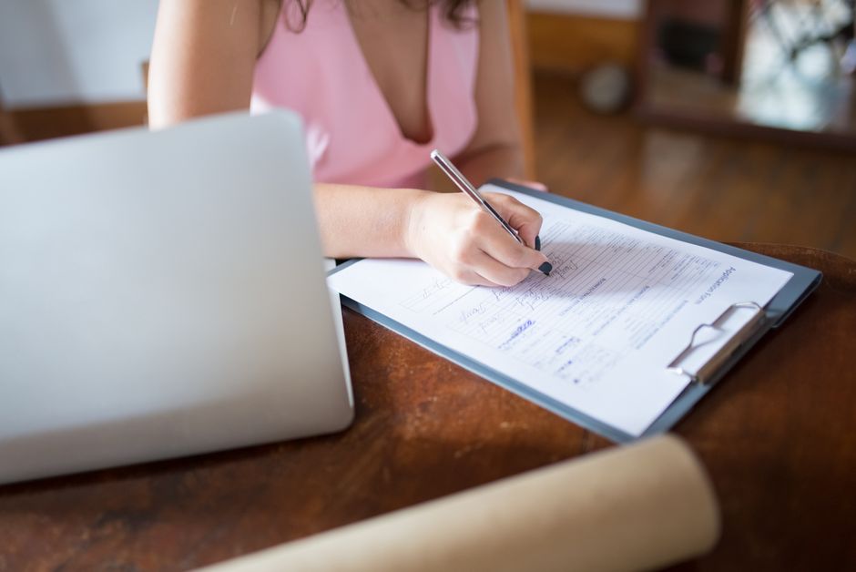 Woman filling in a paper form on a clipboard with a pen, checking details carefully